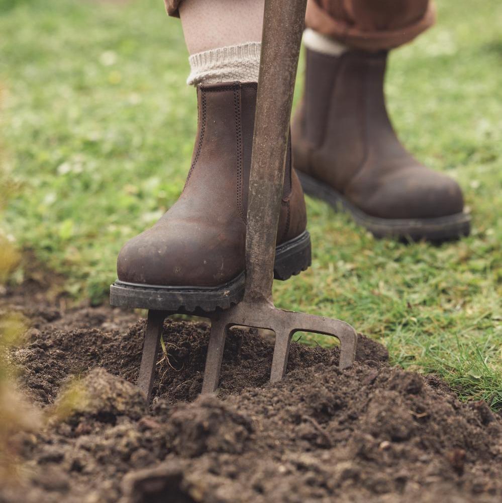 Woman's boot on top of a gardening fork in the ground