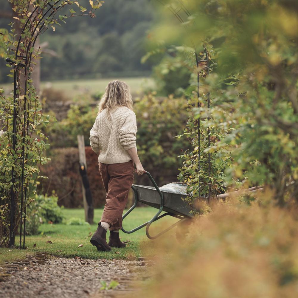 Woman in a garden setting wheeling a wheelbarrow of gardening tools